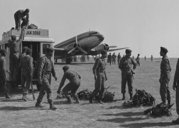 Indian Army soldiers during the 1947 Kashmir operation unloading equipment from a military truck beside a Douglas C-47 transport aircraft on an airfield, preparing to defend Srinagar during the first Indo-Pak war.